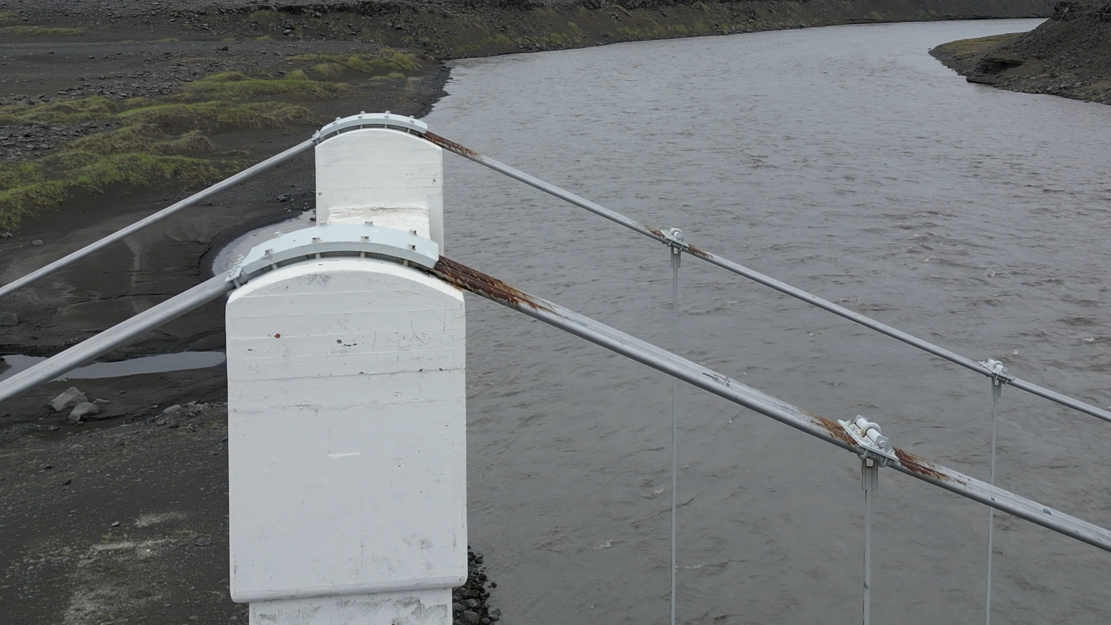 Drone close-up of rusting cables on a suspension bridge over a glacial river