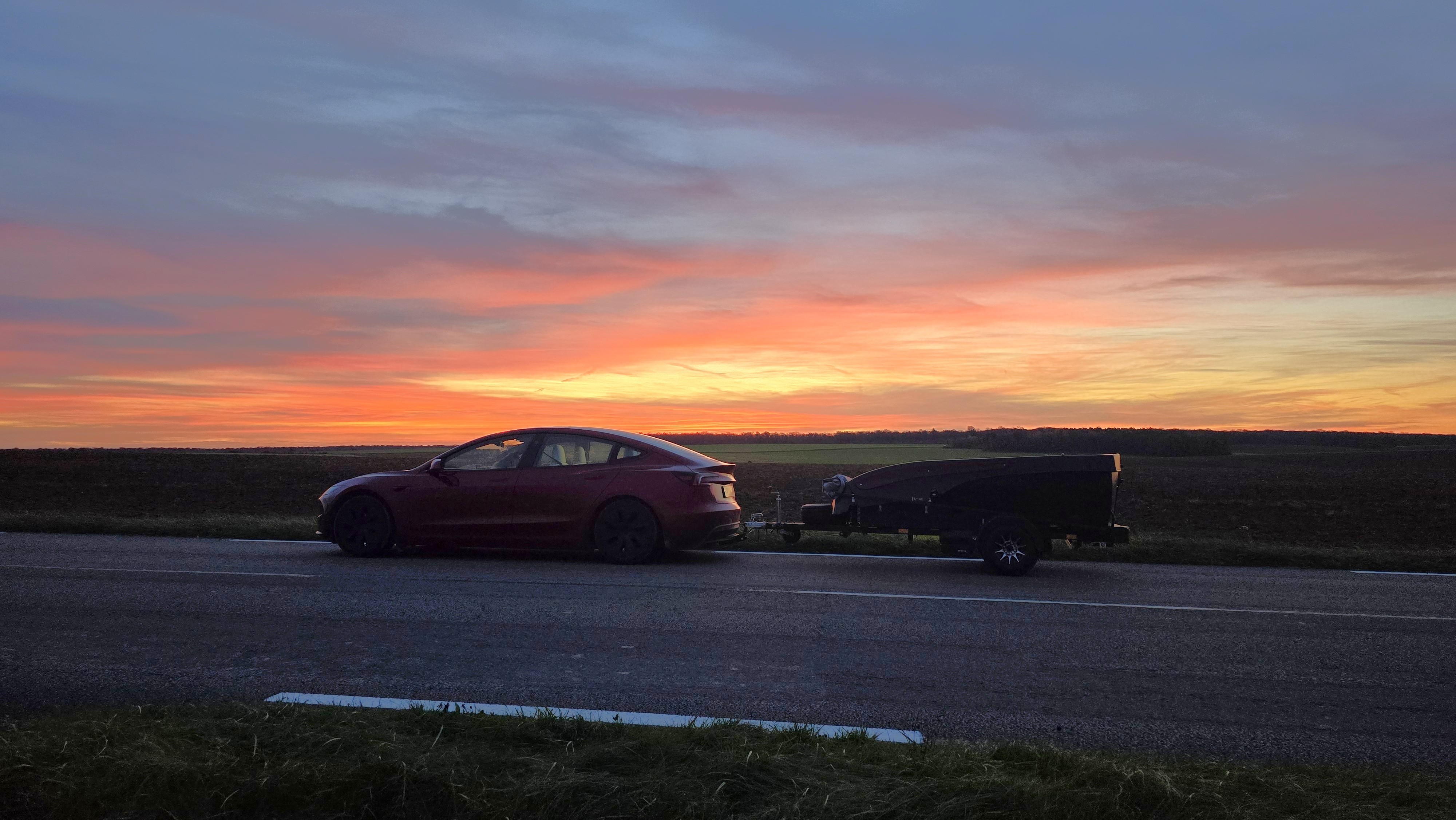Tesla with trailer silhouetted against a sunrise sky in France